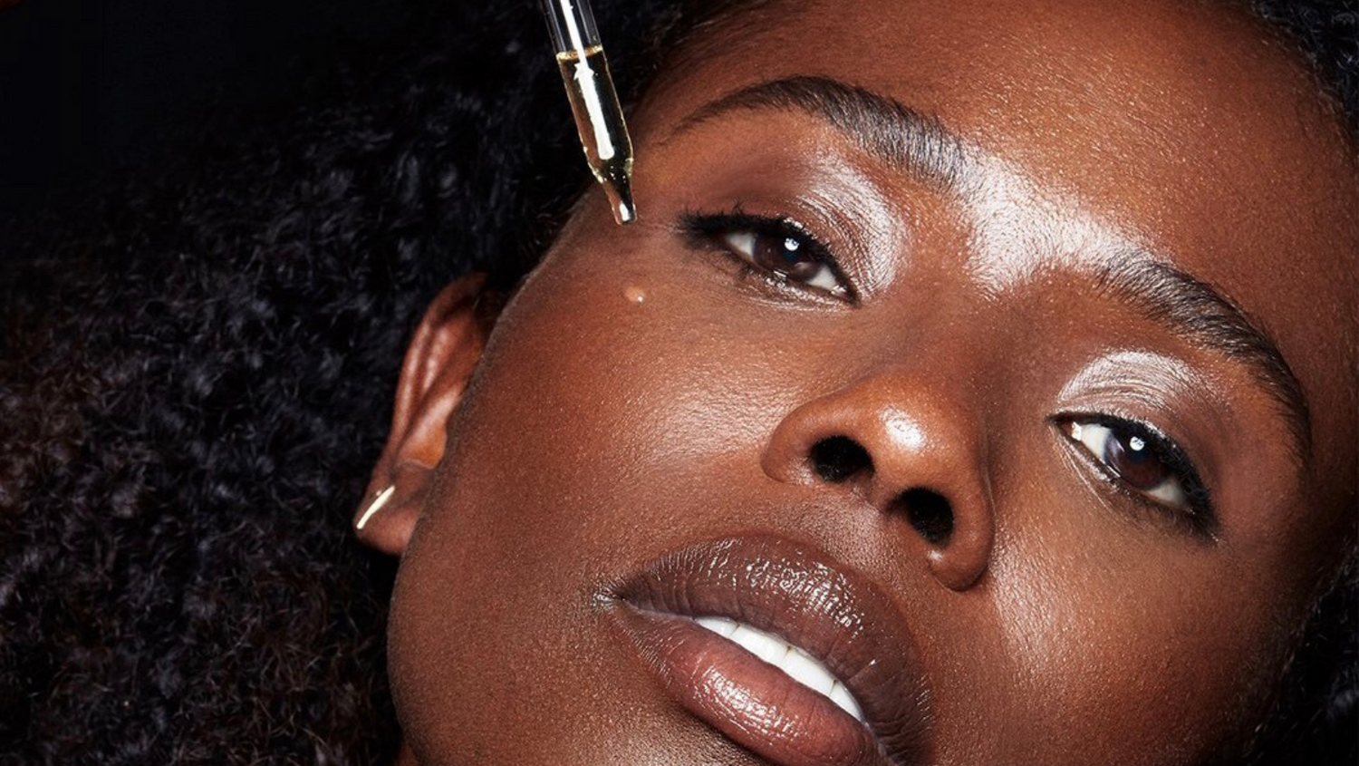 black woman applies hyaluronic skin care sea moss extract serum to her face to improve hyperpigmentation, dryness, and to diminish signs of aging.